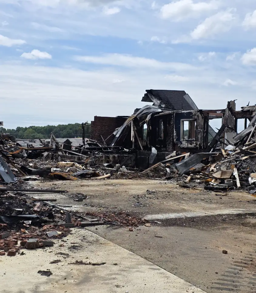 Burned-out house and debris seen across a concrete drive before tear-down