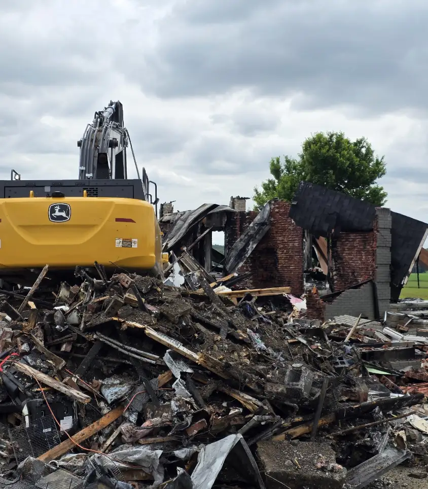 John Deere excavator working through brick and timber debris of a burned house