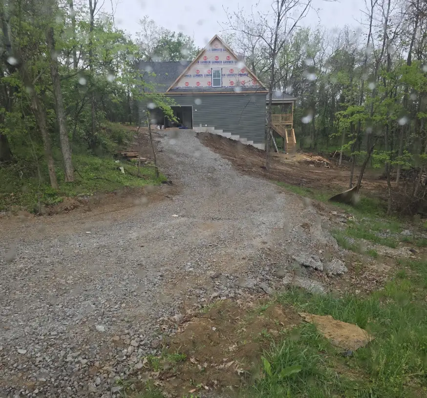 Gravel drive running up a wooded slope to a house under construction